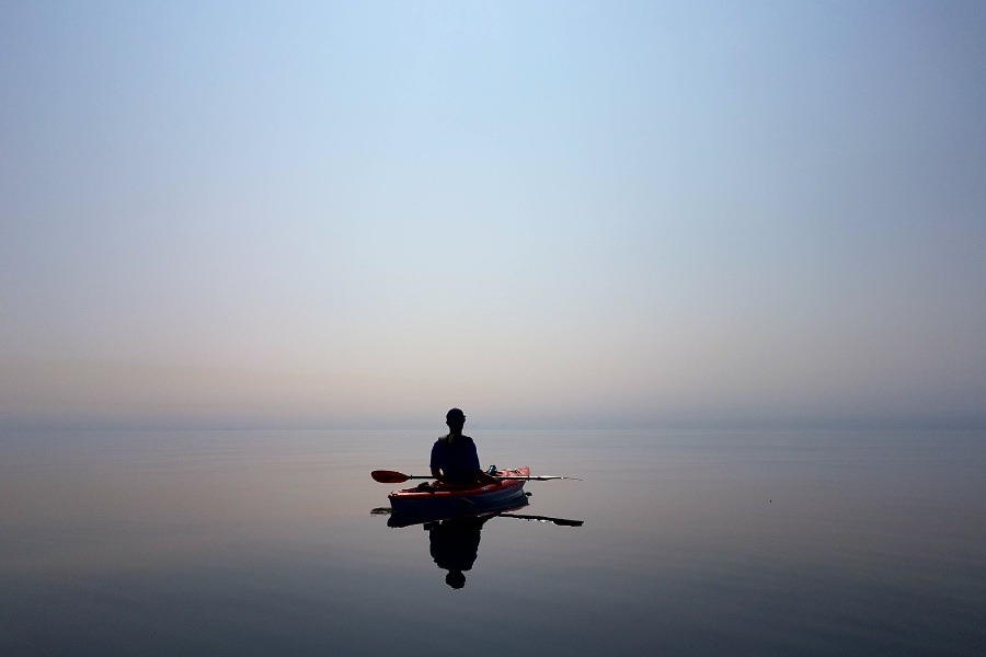 A person sitting in a kayak on still water with blue and purple hues blending between water and sky.